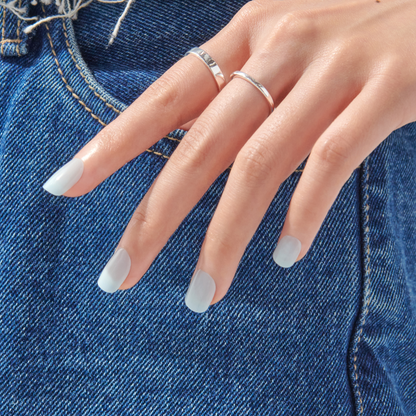 A hand displaying false nails in short squoval shapes in an icy blue color