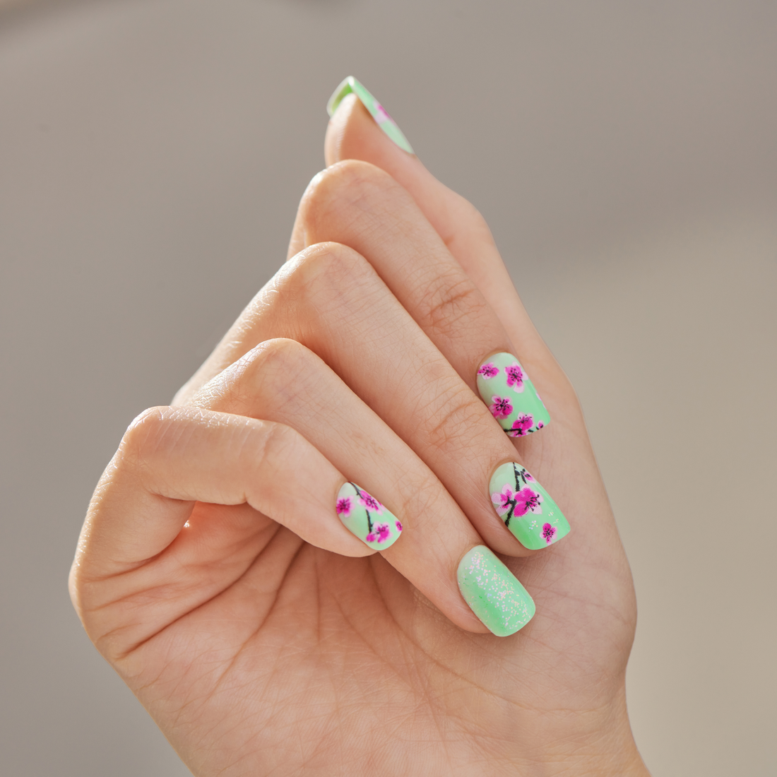A hand displaying Arizona Tea X imPRESS nails with a green background and cherry blossom designs
